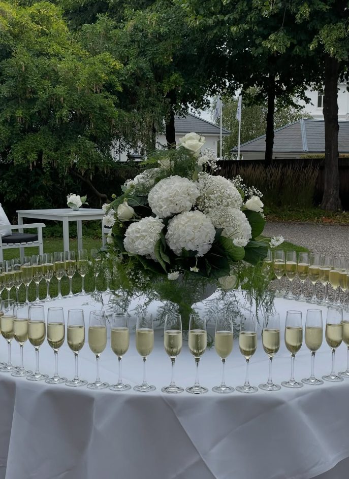 Champagne glasses around a large white flower arrangement in the garden