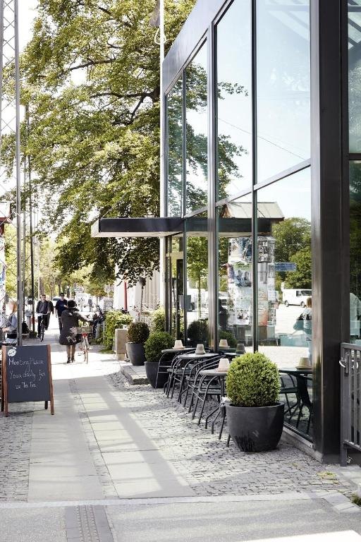 The glass front of Go Hotel Østerport on a tree-lined street with café tables outside