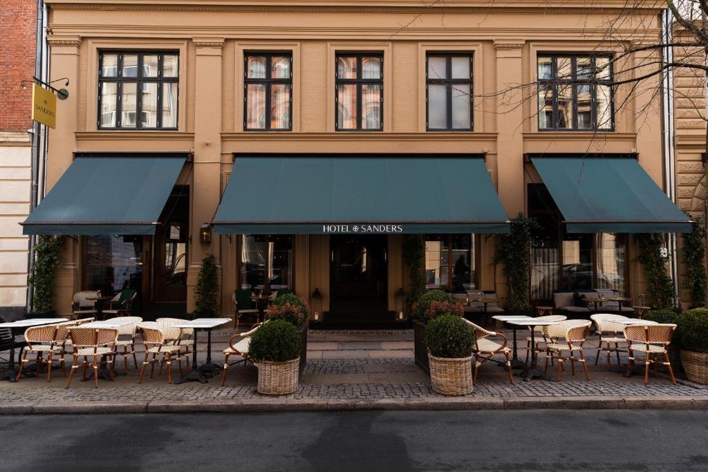 The façade of Hotel Sanders with green awnings and café tables on the pavement